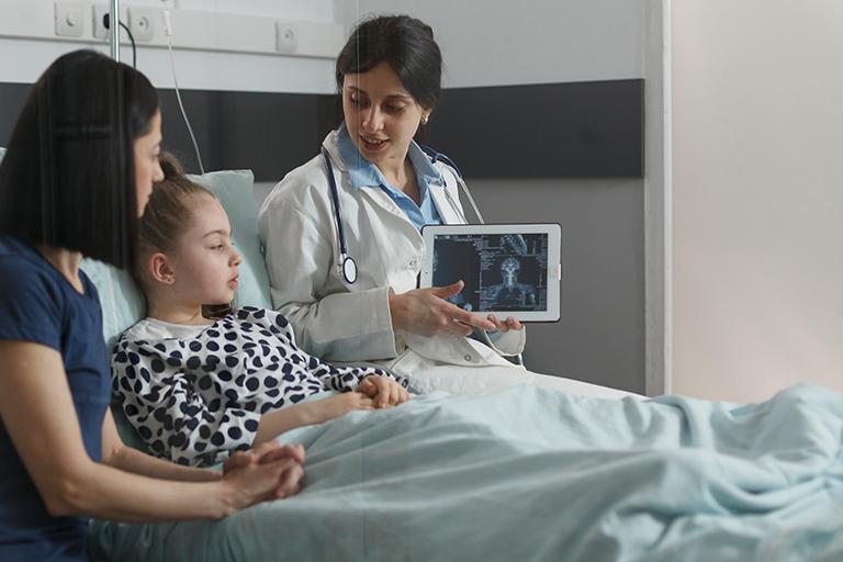 Radiology expert examining radiography scan image of sick little girl resting in hospital pediatric ward. radiologist showing x-ray scanning result of under treatment kid brain condition.