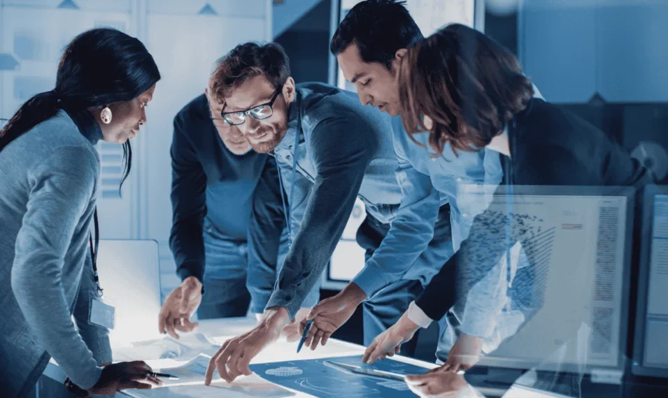 Four colleagues standing around a table working together on a project